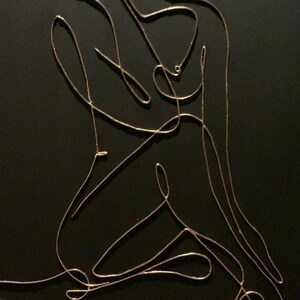 May include: A minimalist artwork featuring a golden wire sculpture of a seated figure against a black background. The continuous line art depicts the form with elegant simplicity, creating a modern and abstract aesthetic.