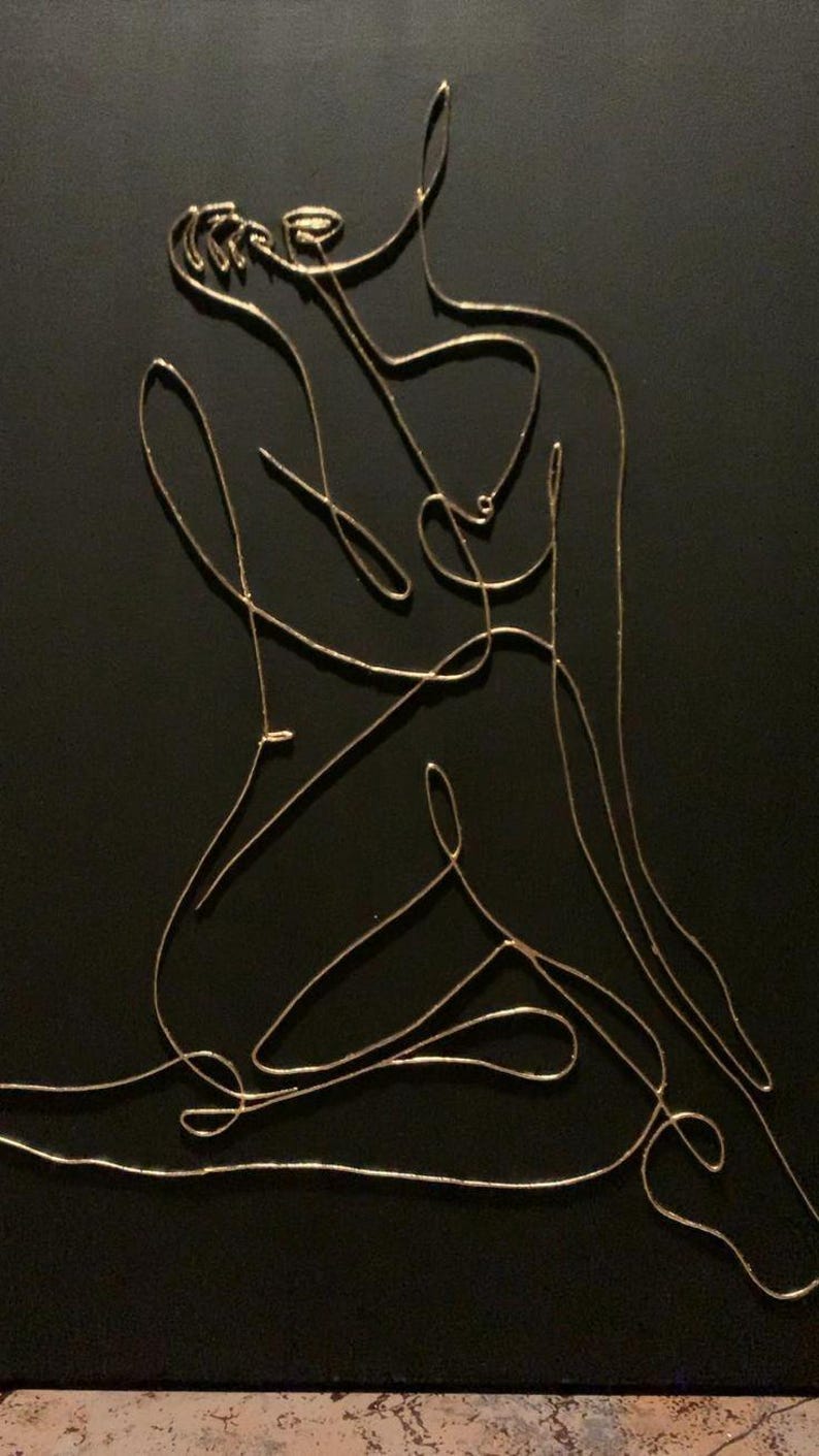 May include: A minimalist artwork featuring a golden wire sculpture of a seated figure against a black background. The continuous line art depicts the form with elegant simplicity, creating a modern and abstract aesthetic.