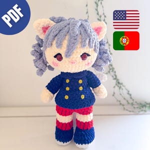 May include: A handmade crochet doll featuring light blue hair, cat ears, and dark red eyes. The doll wears a dark blue jacket with six yellow buttons and red and white striped pants with dark blue shoes. The doll has pink blush on its cheeks.
