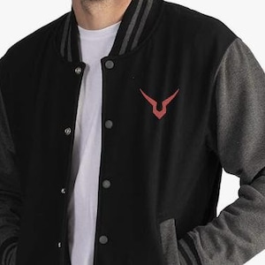 Peut inclure: Veste universitaire noire et grise avec un emblème rouge sur la poitrine. La veste a des manches grises, un corps noir et une bordure rayée grise et noire sur le col, les poignets et l'ourlet. Elle a une fermeture à boutons et des poches.