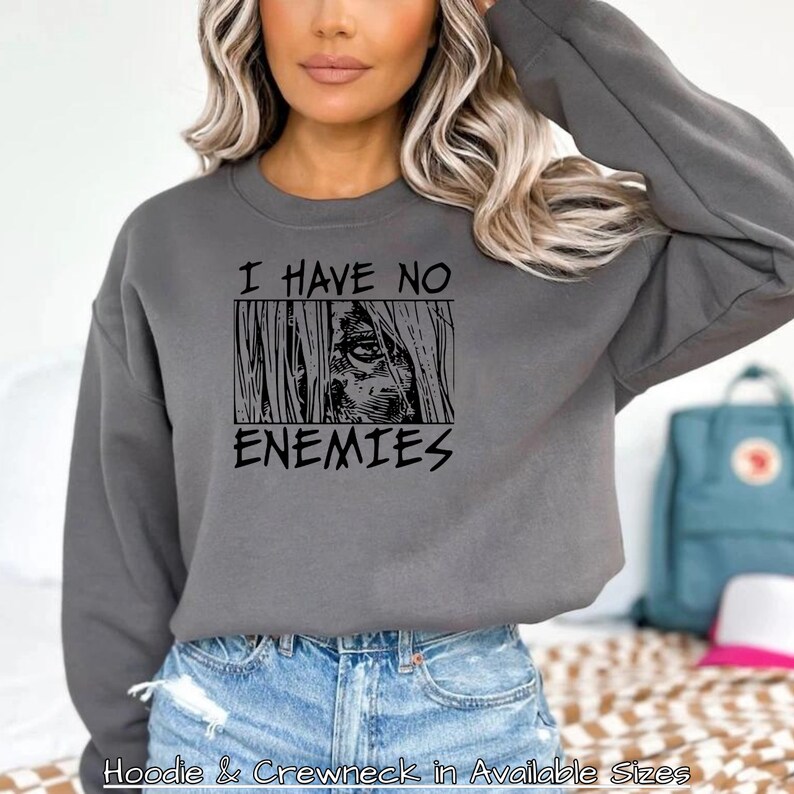 May include: Grey sweatshirt with a black graphic print that says "I have no enemies" with a stylised image of a person's eye looking out from behind bars.