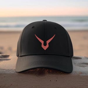 May include: Black baseball cap with a curved peak. The cap has a coral-coloured emblem on the front. The background shows a beach scene with the sea and sky.
