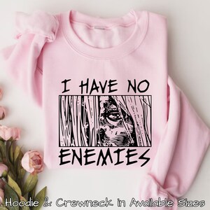 May include: Pink sweatshirt with black text that reads "I have no enemies" and a black and white illustration of an eye.