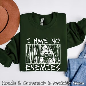 May include: A dark green sweatshirt with white text that reads "I have no enemies" and a graphic of a face behind bars.