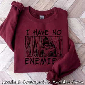 May include: Burgundy sweatshirt with black text that reads "I have no enemies" and a black and white graphic of a person's face with long hair.