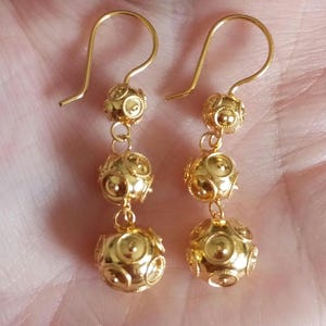 Könnte beinhalten: Ein Paar goldene Ohrhänger mit drei runden, strukturierten Kugeln an jedem Ohrring.