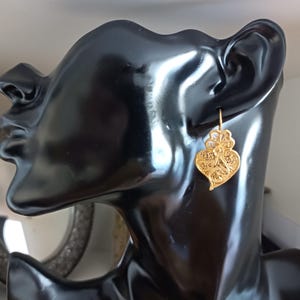 Pu&ograve; includere: Orecchini a forma di cuore in filigrana d'oro. Gli orecchini sono appesi all'orecchio di un manichino.