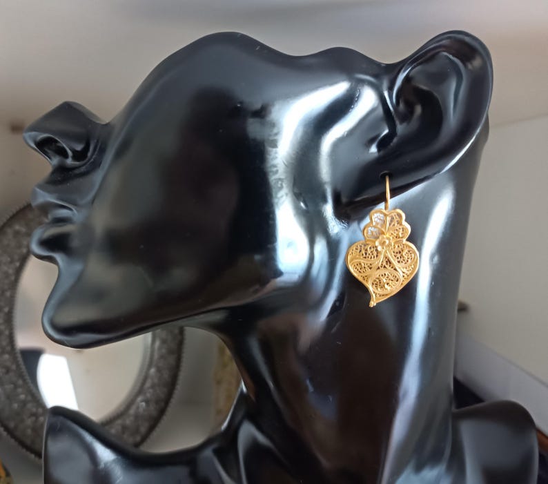Pu&ograve; includere: Orecchini a forma di cuore in filigrana d'oro. Gli orecchini sono appesi all'orecchio di un manichino.