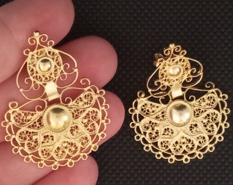 May include: A pair of gold filigree earrings with a delicate, intricate design. The earrings are shaped like a crescent moon with a small circle in the center.