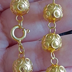 Pu&ograve; includere: Una collana a catena d'oro con perline rotonde e testurizzate. Le perline hanno un motivo circolare.