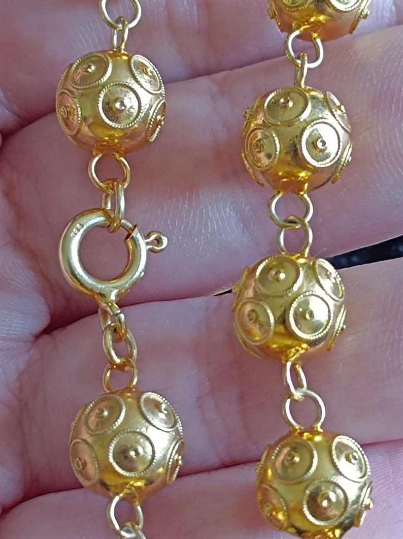 Pu&ograve; includere: Una collana a catena d'oro con perline rotonde e testurizzate. Le perline hanno un motivo circolare.