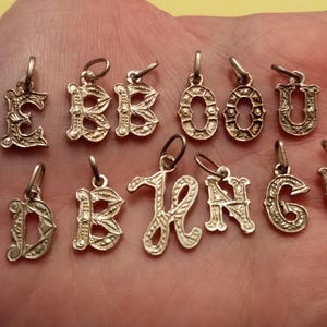 May include: A set of 11 gold-toned metal letter charms, each featuring a different letter of the alphabet in a decorative, ornate style. The charms are perfect for adding a personalized touch to jewelry or crafts.