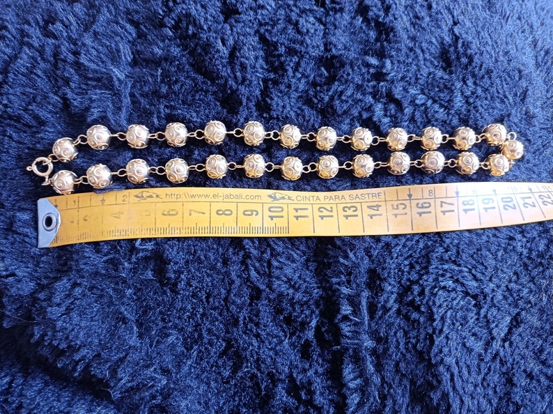 Pu&ograve; includere: Una collana a catena d'oro con perline rotonde e testurizzate. La collana &egrave; misurata con un metro a nastro, mostrando che &egrave; lunga circa 38 cm.