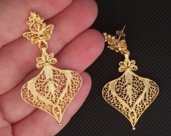 May include: A pair of gold filigree earrings with a butterfly design. The earrings are delicate and intricate, with a floral pattern.