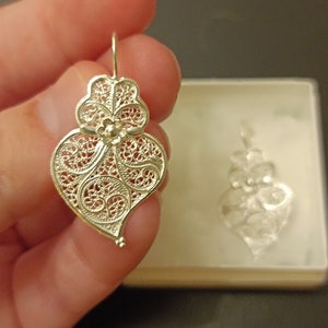 Pu&ograve; includere: Un paio di orecchini a forma di cuore in filigrana d'argento. Gli orecchini sono delicati e intricati, con un motivo floreale al centro. Gli orecchini sono appesi a un gancio d'argento.