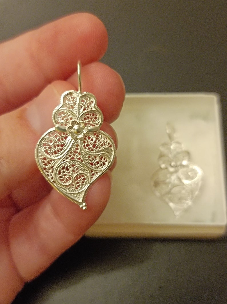 Pu&ograve; includere: Un paio di orecchini a forma di cuore in filigrana d'argento. Gli orecchini sono delicati e intricati, con un motivo floreale al centro. Gli orecchini sono appesi a un gancio d'argento.