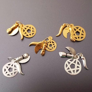 Puede incluir: Cinco amuletos de oro y plata con un diseño de estrella de seis puntas. Cada amuleto tiene una combinación diferente de pequeños amuletos unidos, incluyendo una mano, un cuerno y un ala.