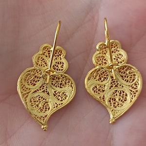 Pu&ograve; includere: Un paio di orecchini a forma di cuore in filigrana dorata con un design delicato e intricato. Gli orecchini sono di stile pendente con chiusura a gancio.