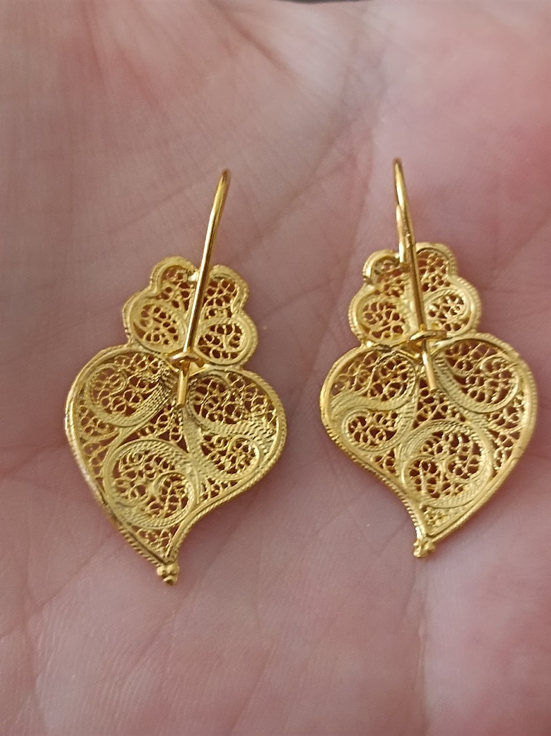 Pu&ograve; includere: Un paio di orecchini a forma di cuore in filigrana dorata con un design delicato e intricato. Gli orecchini sono di stile pendente con chiusura a gancio.