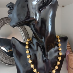 Pu&ograve; includere: Una collana d'oro con perline rotonde e testurizzate su un busto di manichino nero.