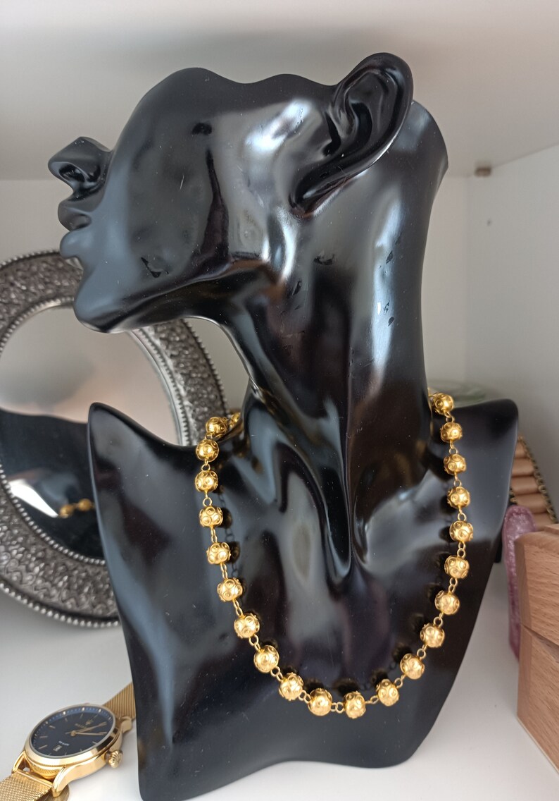 Pu&ograve; includere: Una collana d'oro con perline rotonde e testurizzate su un busto di manichino nero.