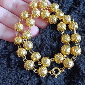 Pu&ograve; includere: Una collana d'oro con una catena e perline rotonde. Le perline hanno una superficie testurizzata con piccoli cerchi.