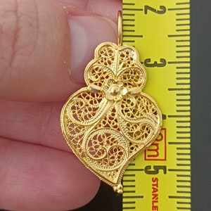 Pu&ograve; includere: Un ciondolo a forma di cuore in filigrana dorata con dettagli intricati. Il ciondolo &egrave; lungo circa 5 cm.
