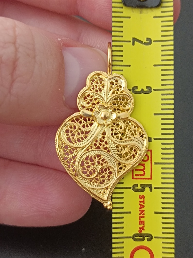 Pu&ograve; includere: Un ciondolo a forma di cuore in filigrana dorata con dettagli intricati. Il ciondolo &egrave; lungo circa 5 cm.