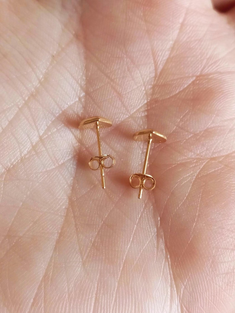 May include: A pair of small gold-toned stud earrings featuring a heart-shaped design. Each earring has a thin post and a secure butterfly-style back closure, showcasing a polished metallic finish that reflects light across the surface.