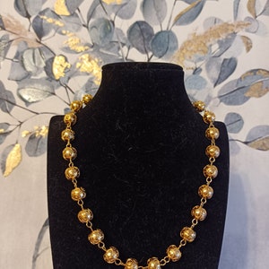 Pu&ograve; includere: Una collana d'oro con perline rotonde e ornate. La collana &egrave; esposta su un supporto in velluto nero.