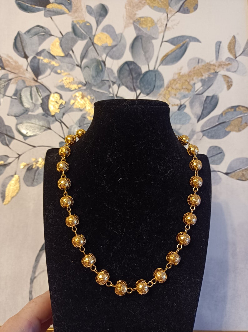Pu&ograve; includere: Una collana d'oro con perline rotonde e ornate. La collana &egrave; esposta su un supporto in velluto nero.
