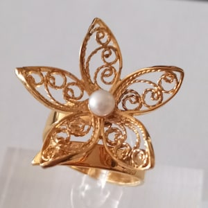 May include: A gold filigree ring with a pearl in the center, shaped like a flower.