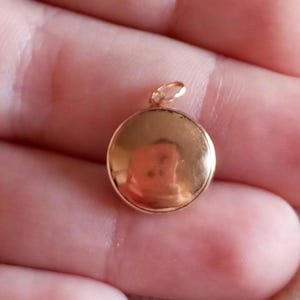 以下が含まれることがあります： 滑らかな表面を持つ丸い金色のペンダント。ペンダントの上部にチェーンに取り付けるためのループがあります。