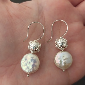 May include: A pair of silver earrings with a round pearl and a silver ball with a textured design.
