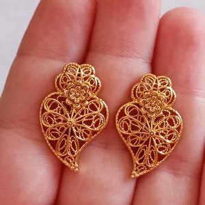Puede incluir: Un par de pendientes de corazón de filigrana dorada con un diseño floral.