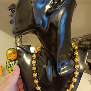 Pu&ograve; includere: Una collana d'oro con perline rotonde su un busto di manichino nero. La collana &egrave; in metallo e ha una finitura lucida.