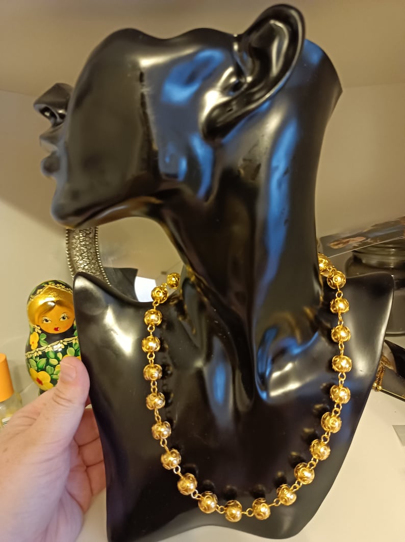 Pu&ograve; includere: Una collana d'oro con perline rotonde su un busto di manichino nero. La collana &egrave; in metallo e ha una finitura lucida.