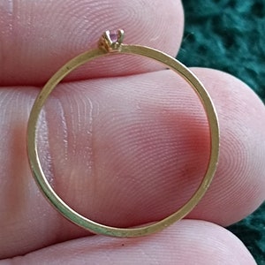 May include: A simple gold band ring with a small pink gemstone set in the center.