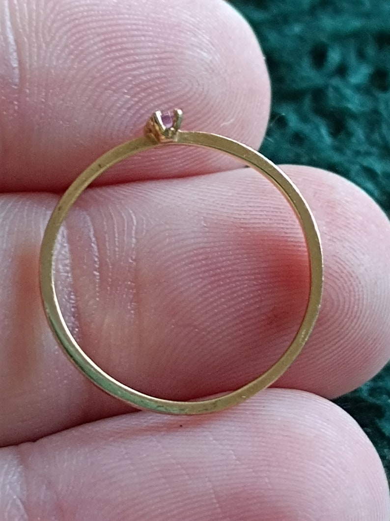 May include: A simple gold band ring with a small pink gemstone set in the center.