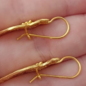 Pu&ograve; includere: Un paio di orecchini d'oro con un design delicato e curvo. Gli orecchini hanno una semplice chiusura a gancio di filo.
