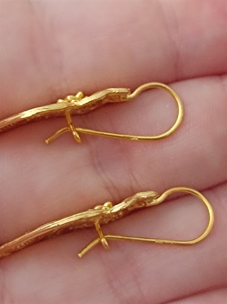 Pu&ograve; includere: Un paio di orecchini d'oro con un design delicato e curvo. Gli orecchini hanno una semplice chiusura a gancio di filo.