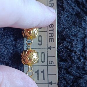 Pu&ograve; includere: Primo piano di una collana a catena dorata con perline rotonde e testurizzate. Le perline hanno un diametro di circa 2,5 cm. La collana viene misurata con un righello, mostrando che le perline sono lunghe tra 23 e 28 cm.