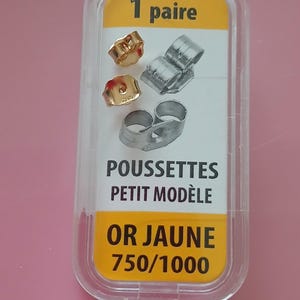 May include: A clear plastic package containing earring backs. The package has a yellow label with the text "1 paire", "POUSSETTES PETIT MODÈLE", and "OR JAUNE 750/1000". The earring backs are gold and silver in color.