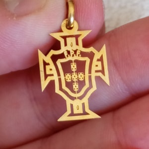 May include: Gold pendant in the shape of a cross with a shield in the center. The shield has the Portuguese coat of arms with the inscription "F.P.F."