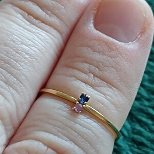 May include: A gold ring with three small gemstones. The gemstones are blue, pink, and pink.