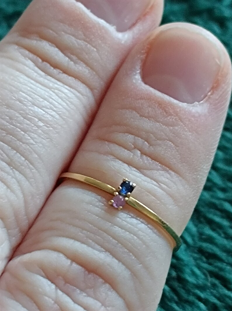 May include: A gold ring with three small gemstones. The gemstones are blue, pink, and pink.