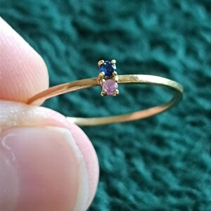 May include: A delicate gold ring with a small blue gemstone and a pink gemstone.