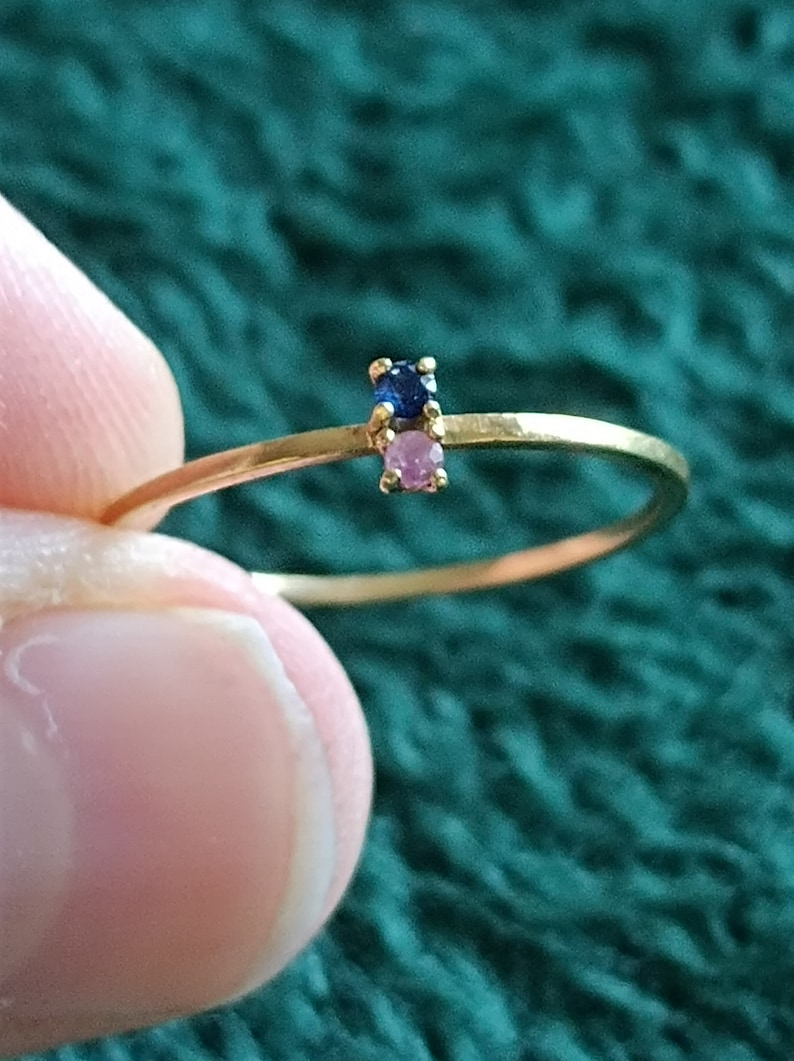 May include: A delicate gold ring with a small blue gemstone and a pink gemstone.