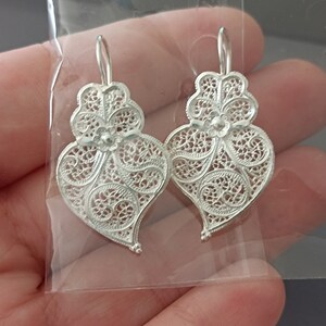 Pu&ograve; includere: Un paio di orecchini a forma di cuore in filigrana d'argento con un delicato motivo floreale.