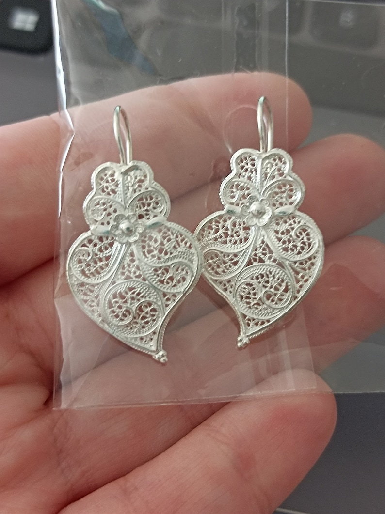 Pu&ograve; includere: Un paio di orecchini a forma di cuore in filigrana d'argento con un delicato motivo floreale.